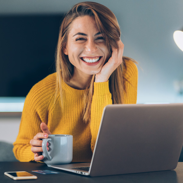woman in yellow sweater with coffee and laptop smiling