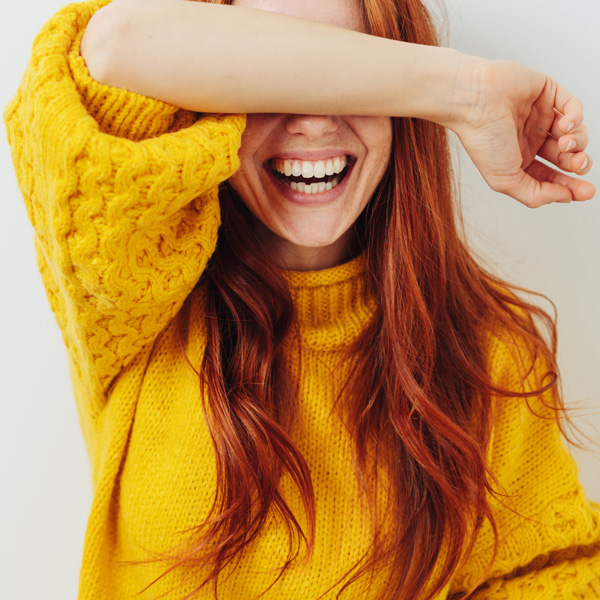 young woman in yellow sweater laughing and covering eyes